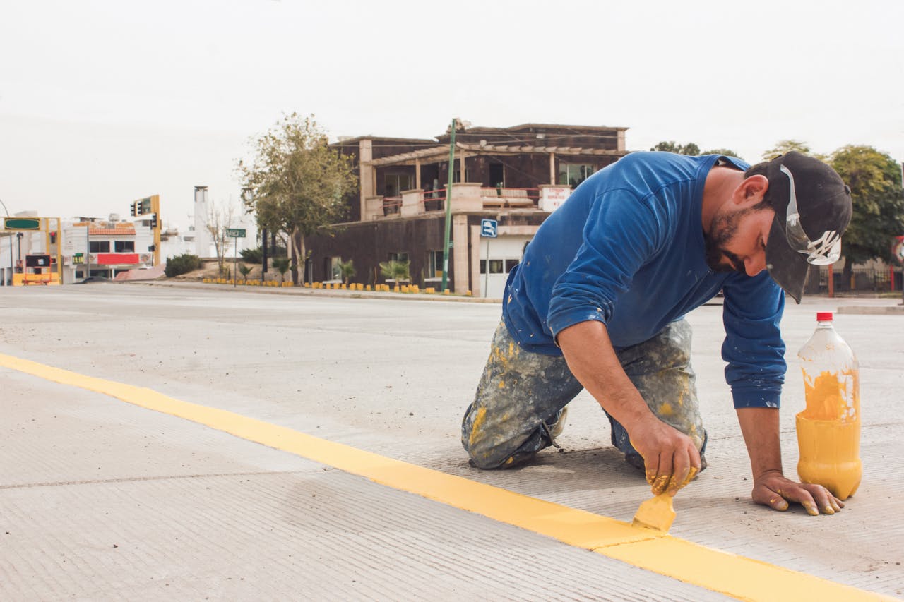 services-02 A man paints yellow road lines on an urban street, emphasizing urban infrastructure and maintenance.