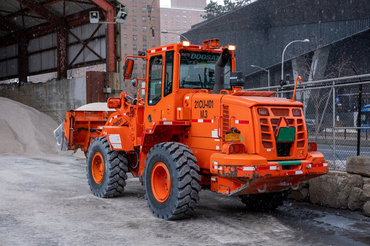 about-us Orange loader vehicle engaged in snow removal in a city environment during winter.