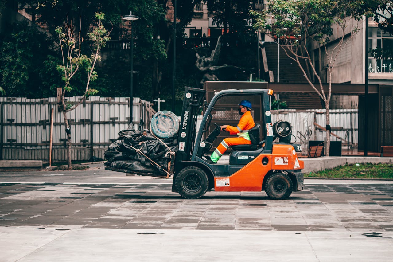 who-we-are A man operates a forklift carrying rubbish in an urban environment, showcasing industrial logistics.